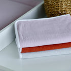 Drei pastellfarbene Handtücher in Rosa, Orange und Grau werden von einem geflochtenen Korb und der KraftKids Wickelunterlage Doppelkrepp Rosa gestapelt - ideal für die Bedürfnisse Ihres Babys beim Wickeln.