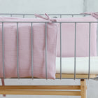 Das KraftKids Bettumrandung Nestchen Doppelkrepp Rosa ist ein modernes Babybett mit Metallrahmen, handgefertigt aus 100 % Baumwolle in zartem Rosa, mit weißer Matratze und hellem Holzsockel vor hellgrauem Hintergrund.