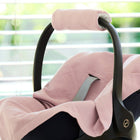 Ein schwarzer Kinderautositz mit der KraftKids Babydecke für Babyschale Sommer Doppelkrepp Rosa in der Nähe eines Fensters mit weichem Tageslicht.