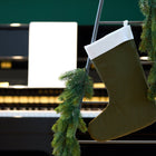 Eine KraftKids Weihnachtssocke Doppelkrepp Grün Herbstgrün und eine Tannengirlande hängen an einer Metallleiter vor einem Klavier mit Notenblättern und bilden die perfekte festliche Weihnachtsdeko.