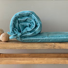 Eine aufgerollte Bettumrandung Nestchen Cord Breitcord Mint von KraftKids liegt auf einer Holzbank neben drei runden Holzkugeln, alle vor einer schlichten grauen Wand.