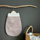 Ein weicher, grauer Cord-Strampelsack Frühling Sommer Cord Breitcord Grau von KraftKids mit weißem Bund hängt an einem Holzast vor einer dunklen Wand. In der Nähe steht ein geflochtener Korb, in dem leichter Stoff sanft drapiert ist.