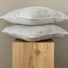 Zwei KraftKids Kissenbezüge Cord Breitcord Beige Taupe (40x40 cm) sind auf einem Holzblock vor einer einfarbig beigen Wand gestapelt und verleihen jeder Bettwäschesammlung subtilen Charme.