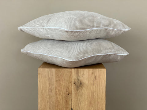 Zwei KraftKids Kissenbezüge Cord Breitcord Beige Taupe (40x40 cm) sind auf einem Holzblock vor einer einfarbig beigen Wand gestapelt und verleihen jeder Bettwäschesammlung subtilen Charme.