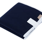 Die KraftKids Reisewickelunterlage Musselin dunkelblau ist eine sauber gefaltete marineblaue Reisewickelunterlage mit weißem Rand und braunem SOUND SLEEP Anhänger, ideal als Wickelauflage für unterwegs, abgebildet auf weißem Hintergrund.