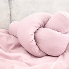 Die KraftKids Wickeltischumrandung Doppelkrepp Rosa wird mit einem Knoten gebunden und auf eine passende rosa Strukturdecke vor einem hellgrauen Betonhintergrund gelegt.